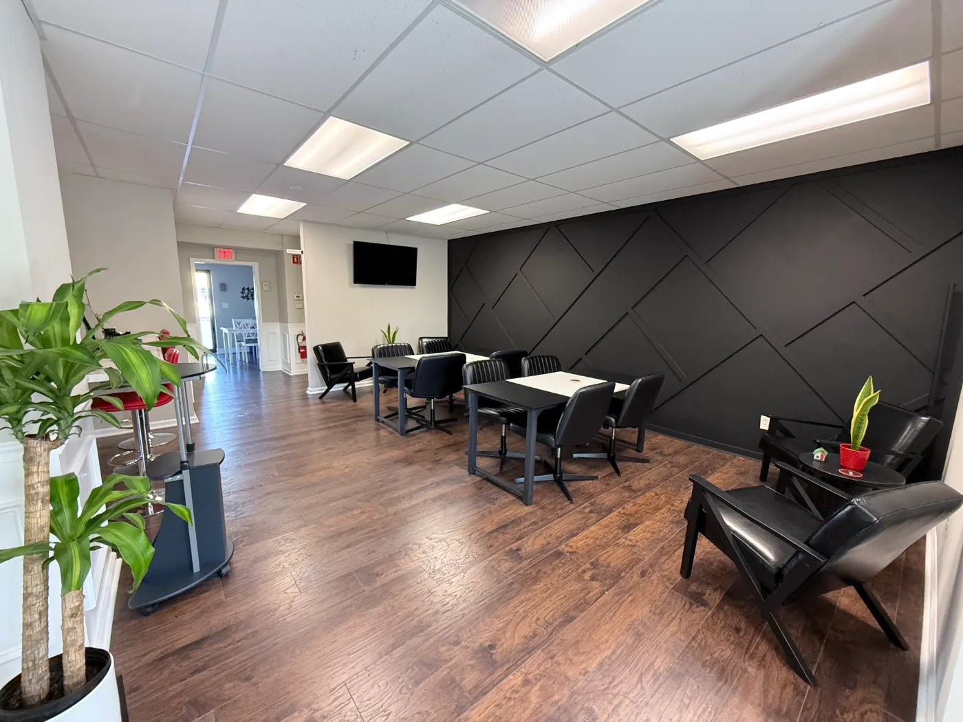OMNI Real Estate Professionals open workspace with tables, lounge seating, and the geometric black accent wall
